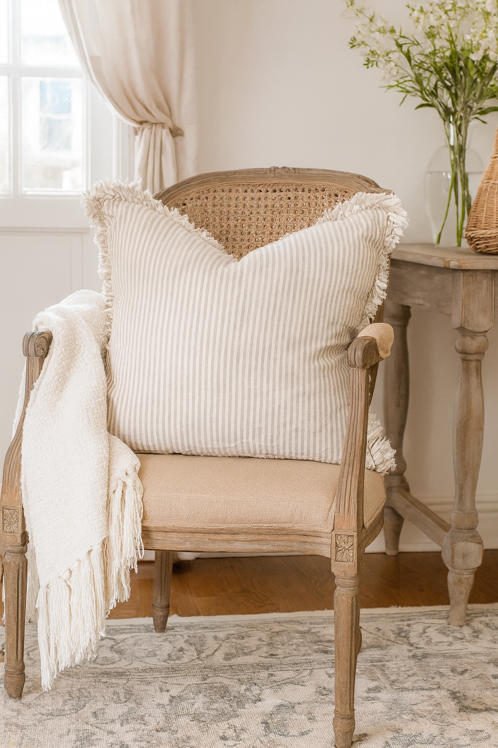 A large striped linen ruffle cushion styled on a rustic country cottage armchair with a soft throw, perfect for cosy farmhouse interiors.