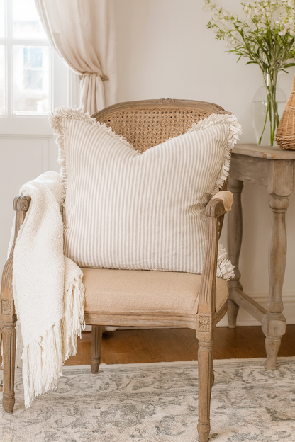 A large striped linen ruffle cushion styled on a rustic country cottage armchair with a soft throw, perfect for cosy farmhouse interiors.