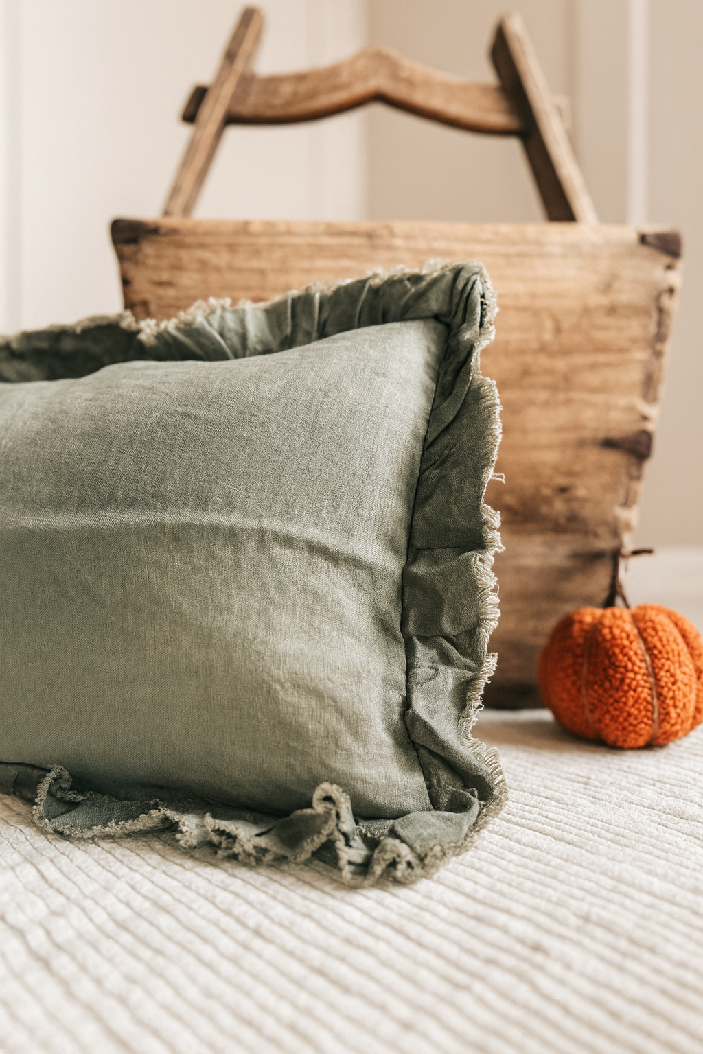 Green cushion with ruffled edges on a textured surface with a wooden basket and orange pumpkin in the background.