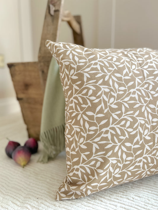 Olive green cushion with white leaf print, styled on a neutral textured background with figs and rustic accents for cozy home interiors.