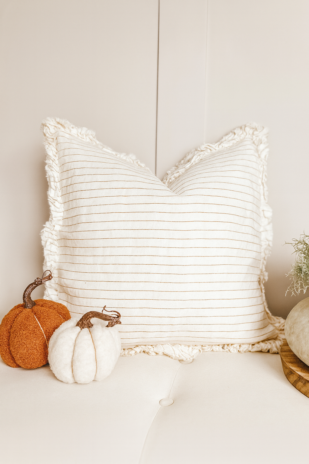 Rust pinstripe linen cushion with ruffle edge on a neutral sofa.