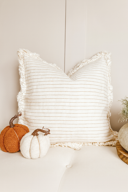Rust pinstripe linen cushion with ruffle edge on a neutral sofa.