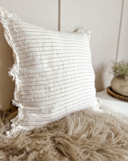Rust striped scatter cushion, 53×53, layered with beige cushions.